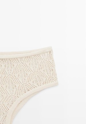 Kremowa koronkowa bielizna z geometrycznymi i kwiatowymi wzorami dzianinowymi, z elastycznym pasem i otworami na nogi na jednolitym białym tle.