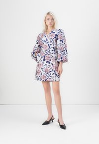 Φλοράλ φόρεμα σε λευκό χρώμα με ροζ και ναυτικό μπλε σχέδια λουλουδιών, με ντεκολτέ σε V, φουσκωτά μανίκια και πλευρικές τσέπες. Συνδυάζεται με μαύρες γόβες με αιχμηρή μύτη.