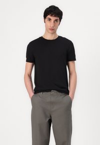 Zwarte korte mouwen t-shirt met een ronde hals, gedragen met lichtgrijze broek. De stof ziet er glad uit met een casual pasvorm en strakke lijnen.