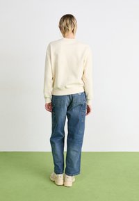 Kerma sweatshirt dengan potongan santai, lengan bertali, dipadukan dengan celana kargo denim biru yang longgar dan dilengkapi dengan saku patch.