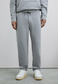 Pantalones deportivos grises hechos de un material suave, con cintura ajustable con cordón, bolsillos laterales y un corte holgado. Combinados con zapatillas blancas.