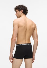 Czarne bawełniane bokserki mają logo na pasku, gładki, dopasowany krój oraz środkowy wysokość. Materiał wydaje się miękki i elastyczny.