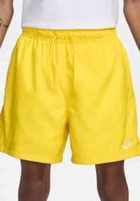 Shorts de bain jaunes avec taille élastique et cordon de serrage. Présente une texture lisse et un petit logo blanc en bas à droite.
