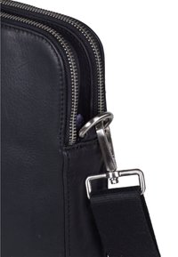 Schwarze Ledertasche mit zwei Reißverschlüssen, silbernem Zubehör und einem abnehmbaren Tragegurt. Besitzt eine glatte Textur und sichtbare Nähte.
