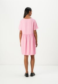 Robe courte rose avec des manches courtes, taille froncée et coupe décontractée. Le tissu semble lisse ; le dos présente un col rond et aucun motif visible.