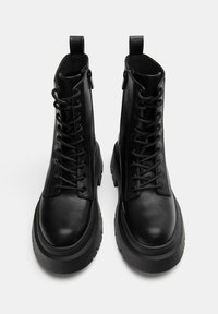 Fekete bőr bokacsizma fűzős kivitelben, kerek orral, vastag talppal és hátsó húzófüllel. Simább textúra és masszív kialakítás.