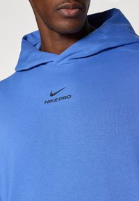 Blue Nike Pro hoodie made of stretchy fabric. Features a front logo and a spacious hood. Smooth texture with a slight sheen.