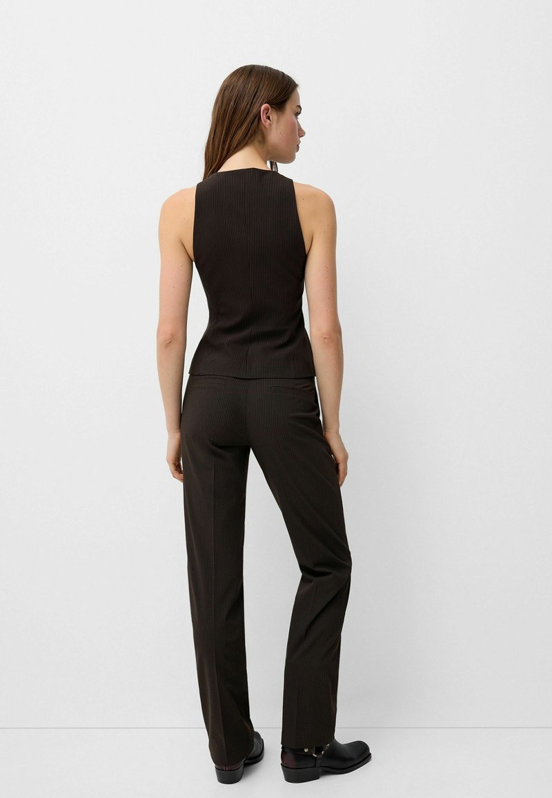 Top senza maniche a costine marroni abbinato a pantaloni pinstripati marroni. Presenta una silhouette aderente e un design minimalista.