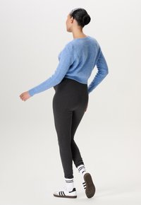 Lichtblauwe cropped sweater met een structuur breiwerk, gecombineerd met donkergrijze leggings. Schoeisel: zwart-witte sneakers met strepen en een gestructureerde zool.