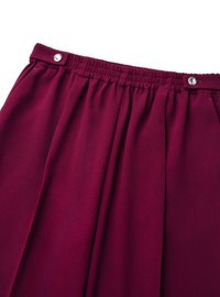 Falda plisada burdeos con cinturilla elástica y cierre de botón a presión. Confeccionada en tela suave. Presenta pliegues verticales para añadir textura.