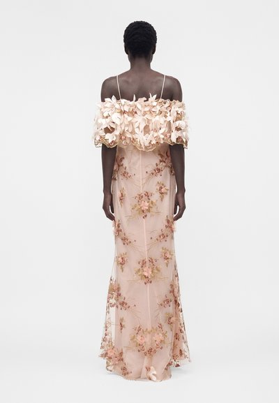 Γυναίκα που φοράει μακρύ φορεματιστό φόρεμα σε ανοιχτό ροζ χρώμα με floral κέντημα και τρισδιάστατες λουλουδένιες λεπτομέρειες στο ντεκολτέ χωρίς ώμους, όρθια με την πλάτη προς το μέρος μας.