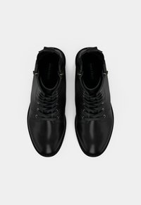 Mustad nahast pahkluu saapad sileda viimistlusega, millel on nöörid ja metallist kaunistused. Ümar varvas ja minimalistik disain.