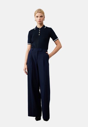 Polo shirt bleu marine à manches courtes avec col et poignets blancs, doté de boutons dorés ; associé à un pantalon bleu marine taille haute et à jambes larges.
