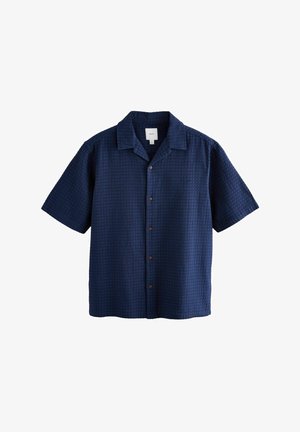 Camicia a maniche corte, blu navy, con un motivo a nido d'ape in rilievo, chiusura frontale a bottoni e colletto classico. Presenta bottoni marroni.