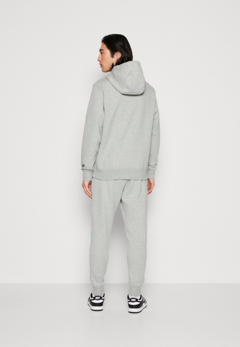 Graue Kapuzenpullover- und Jogginghose-Kombination aus Baumwollmischgewebe, mit vorderer Kängurutasche, verstellbarem Kapuze, gerippten Bündchen und Taillengummi; getragen mit Turnschuhen.