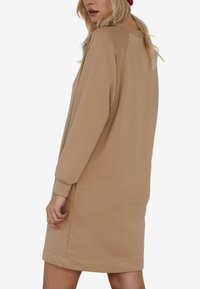 Khaki sukienka dresowa z długimi rękawami, okrągłym dekoltem i ściągaczami. Miękka tekstura i luźny krój z lekko zaokrąglonym dołem.