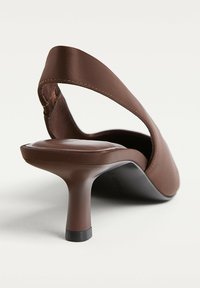 Escarpin marron à talon slingback avec une finition satinée, un bout rond et un talon aiguille fin. La lanière se croise pour un design à dos ouvert.