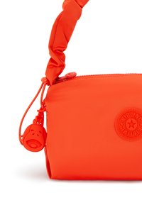 Ljust orange axelväska med en texturerad, mjuk tygkänsla, en knuten rem och en gummimonkey nyckelring för extra detalj.