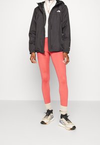 Black waterproof jacket, pink leggings, and multicolored athletic shoes. Jacket has drawstring hood; leggings are fitted; shoes feature textured soles.