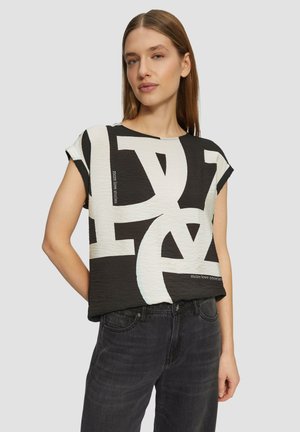 Haut noir à manches courtes avec de grandes lettres blanches et un tissu texturé, à col rond et coupe décontractée. Les accents incluent du texte imprimé.