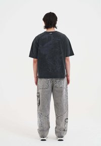 Czarna koszulka z krótkim rękawem z grafiką smoka na plecach, połączona z szarymi dżinsami z białymi detalami i kieszeniami cargo.