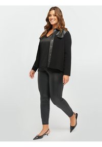 Blazer nero con accenti in pelle sintetica, canotta nera in satin con pizzo, leggings neri simili al lattice e décolleté con punte e borchie.