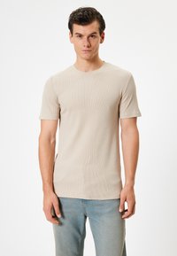Beige ribbet t-shirt med korte ærmer, rund halsudskæring og en tætsiddende pasform, parret med lyseblå jeans. Glat tekstur, minimalistisk design.