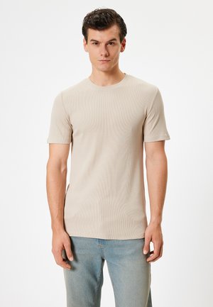 Camiseta de rayas beige con mangas cortas, escote redondo y un ajuste ceñido, combinada con vaqueros de color azul claro. Textura suave, diseño minimalista.