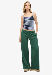 Niebiesko-białe paski bezrękawnik zestawione z ciemnozielonymi szerokimi spodniami dresowymi. Miękka tkanina z elastycznym paskiem w talii oraz swobodny krój.