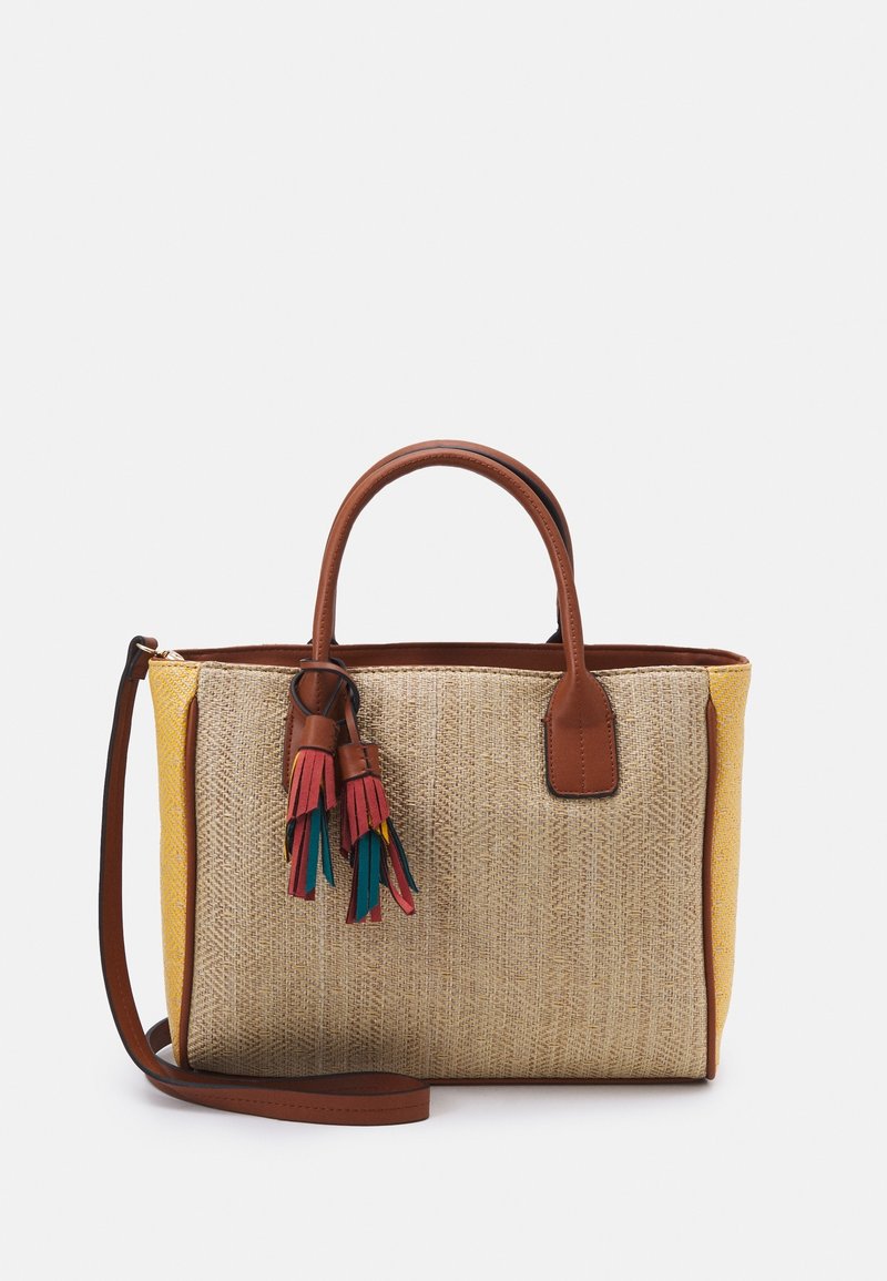 Sac fourre-tout tissé avec une base jaune, des poignées en cuir marron et des pompons colorés. Présente un matériau texturé semblable à de la paille naturelle.