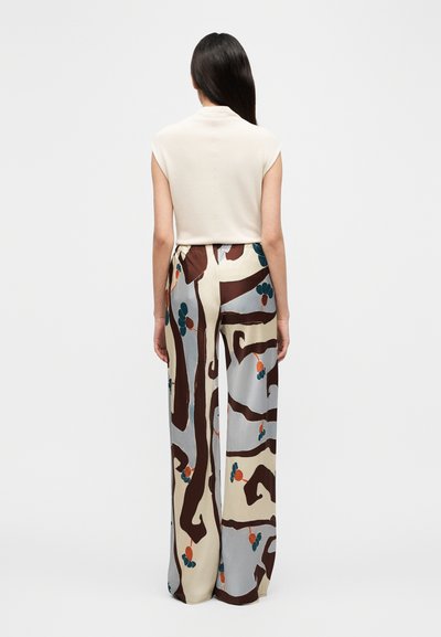 Beige, kortermet topp kombinert med vidt mønstrete bukser med brune, blå og oransje motiver på lys bakgrunn.