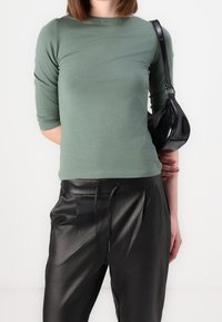 Maglietta a maniche lunghe verde menta con un design aderente, abbinata a pantaloni neri in ecopelle a vita alta con dettagli a coulisse e pieghe.