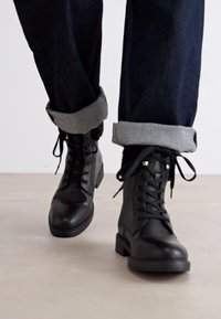Stivaletti neri in pelle con lacci, punta rotonda e tacco a blocco. I jeans presentano un orlo risvoltato con rivestimento grigio.