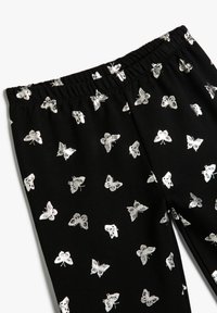 Pantalones con cintura elástica negra y un patrón disperso de pequeñas mariposas plateadas brillantes.