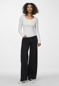 Bílý žebrovaný top s dlouhým rukávem a knoflíkovou légou, spárovaný s černými džínami s vysokým pasem a širokým střihem, a černými teniskami s bílou podrážkou.