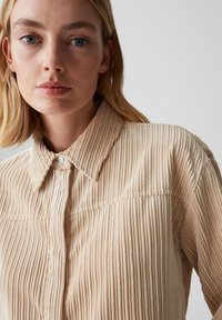 Camicia in corduroy beige con texture a righe verticali, apertura frontale con bottoni e colletto classico. Presenta dettagli di cucitura sottili.
