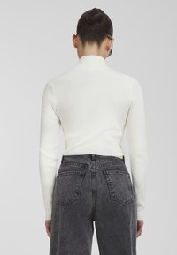 White ribbed long-sleeve top with a high neckline; paired with high-waisted black denim jeans featuring back pockets and a faded texture.