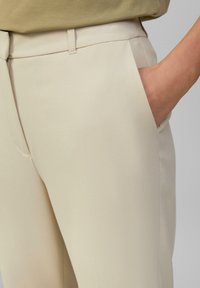Beige op maat gemaakte broek van een textuurstof, met zijzakken en een recht model. Dragen met een lichtgroene top.