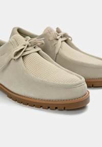 Pantofi din suede bej cu panouri din plasă, design cu șireturi și talpă din cauciuc cu textură pentru aderență. Vârf simplu, rotund, și detalii de cusătură.