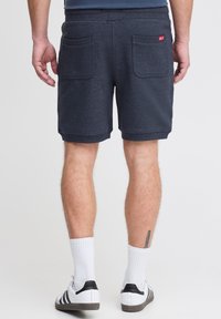 Marinblå shorts i mjukt material, med två bakfickor, elastisk midja och ribbade muddar, tillsammans med vita strumpor och sneakers.