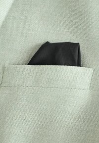 Light green fabric with a textured weave, featuring a black pocket square neatly folded in a chest pocket.