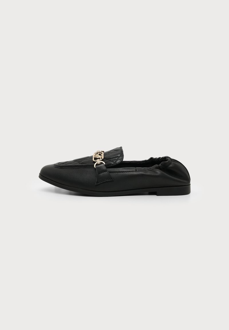 Mocassin plat en cuir matelassé noir avec détail de boucle dorée et talon arrière élastique, vu de côté sur un fond uni.