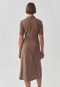 Vestido marrón de media longitud con mangas cortas, diseño ajustado, textura suave y un ligero drapeado en el dobladillo. La vista trasera resalta líneas simples.