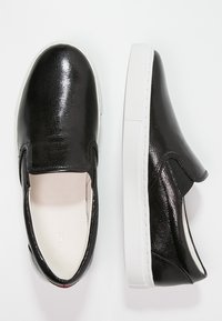 Chaussures noires à enfiler avec une tige synthétique texturée, dotées d'une semelle en caoutchouc blanche lisse et de panneaux latéraux élastiques pour faciliter l'enfilage.