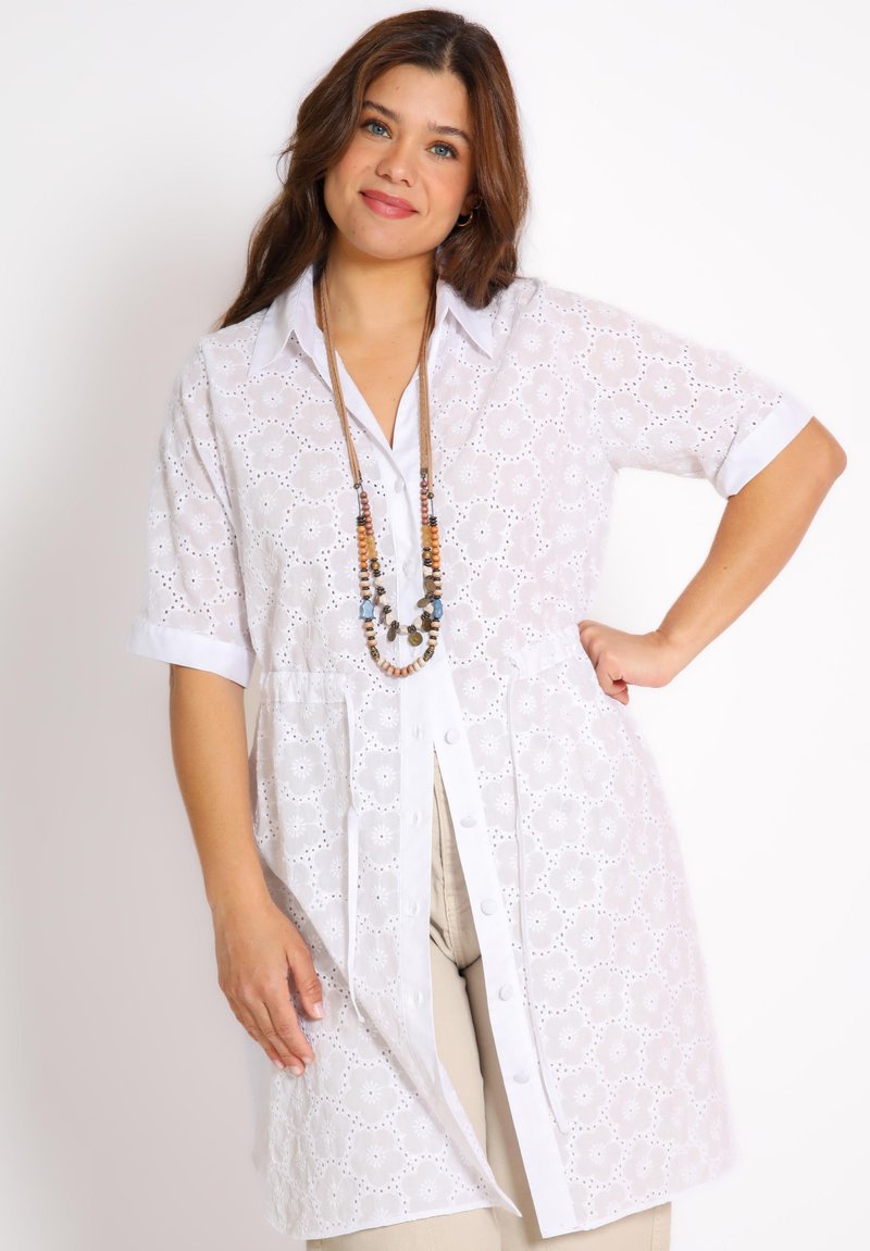 White lace blouse with short sleeves, button-down front, decorative floral cutouts, collar, and a relaxed fit. Includes a beaded necklace.