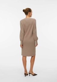 Robe en tricot beige avec de longues manches bouffantes, longueur genoux, col rond et texture côtelée. Associée à des mules à talons bruns.