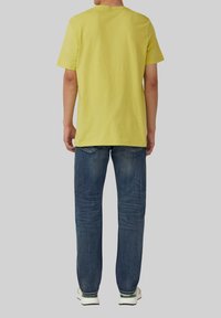 T-shirt en coton jaune à manches courtes et col rond, associé à un jean en denim bleu foncé et des chaussures de sport blanches.