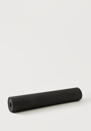 Esterilla de yoga negra enrollada con nombre de marca sutil sobre un fondo claro.
