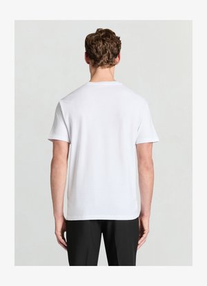 T-shirt blanc en coton avec manches courtes, col rond et texture lisse. Il présente un ourlet droit et est porté avec un pantalon noir.