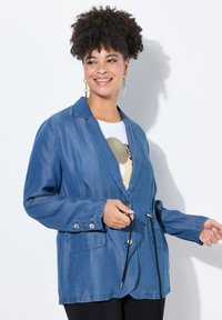 Denimblazer i mellanblått, med slagkrage, två framfickor, knäppning med knappar och justerbar dragsko i midjan.